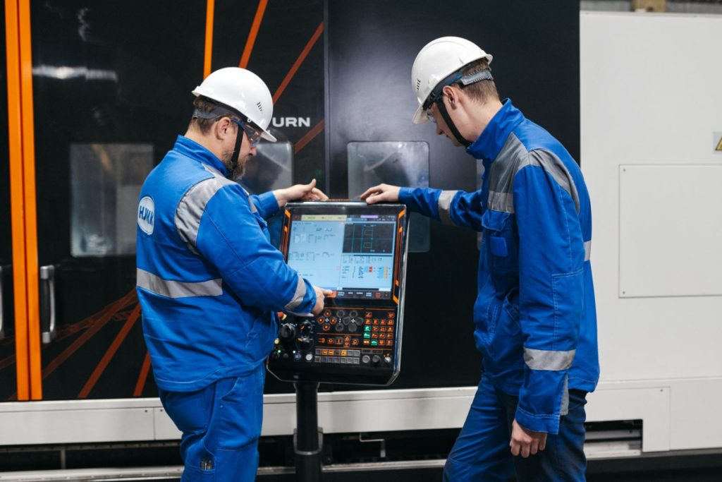 Two engineers operating CNC machinery in a factory setting, wearing safety gear and uniforms.