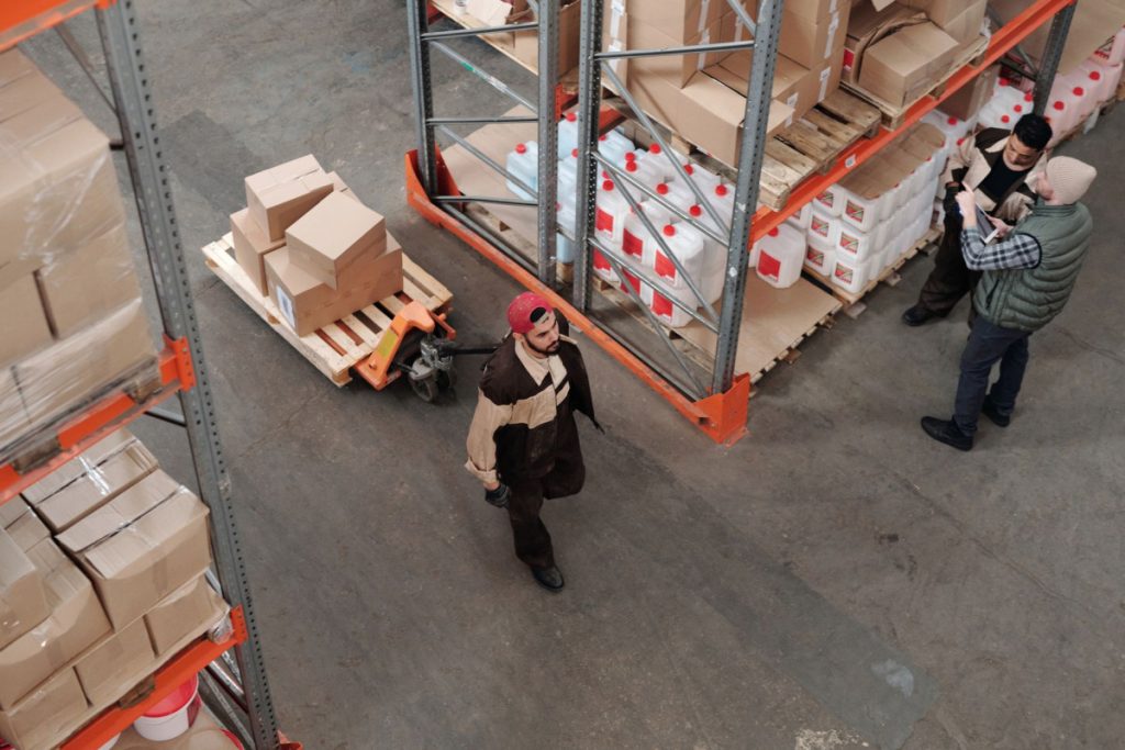 Team working in an industrial warehouse discussing and organizing inventory with pallets.