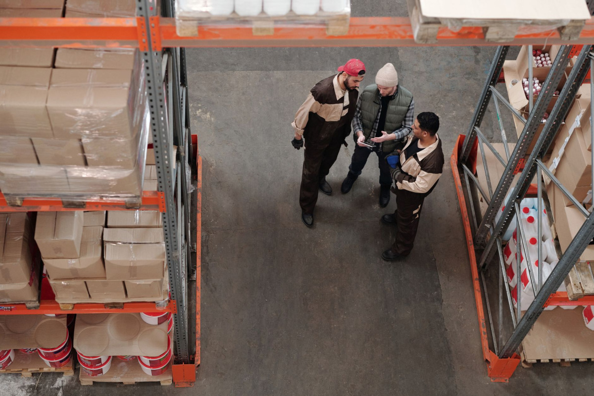 Three warehouse workers discussing logistics in an industrial storage area.